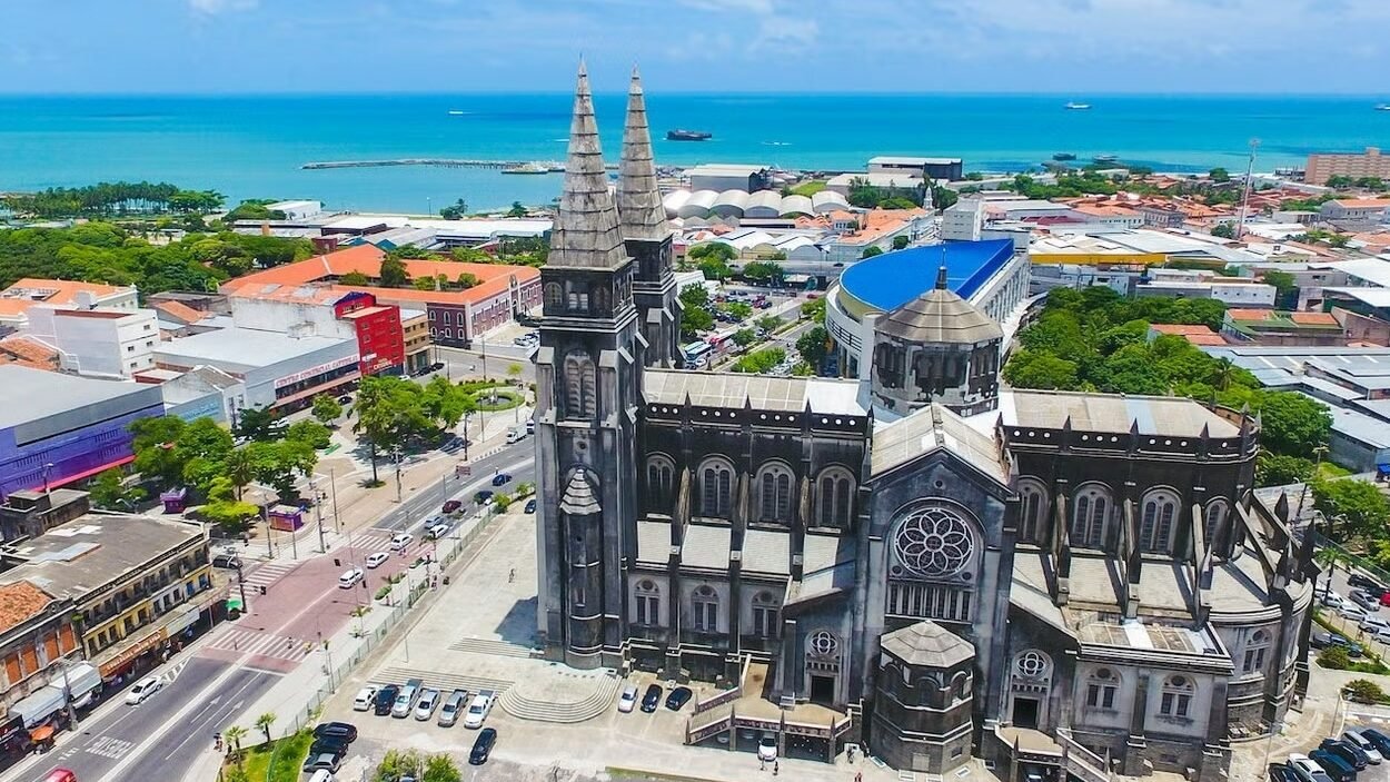 Imagem aérea do centro histórico de fortaleza durante o dia. A catedral metropolitana está em foco. No fundo é possível ver a praia.