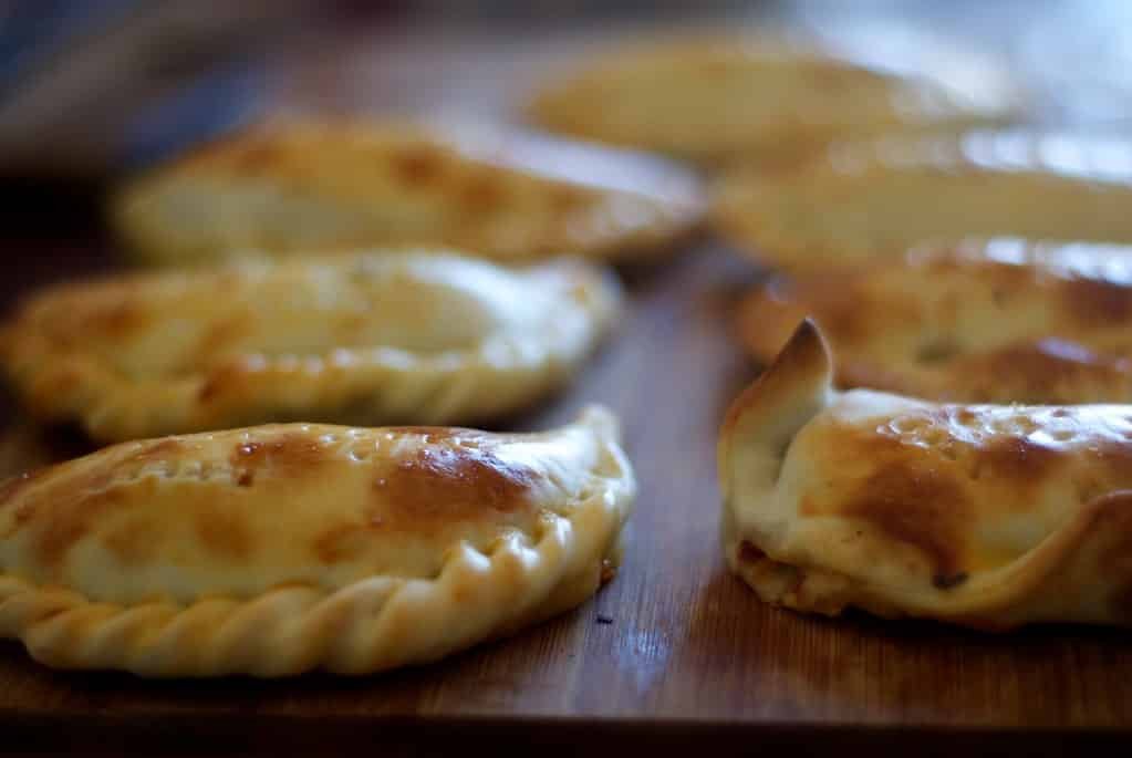 Empanadas caseiras, que parecem um pastel assado em formato de meio círculo com bordas bem trabalhadas