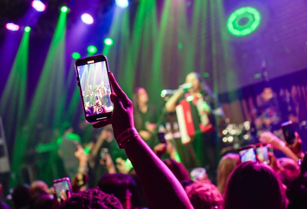 Mão segurando um celular com o show acontecendo ao fundo em Maikai, uma casa noturna em Maceió