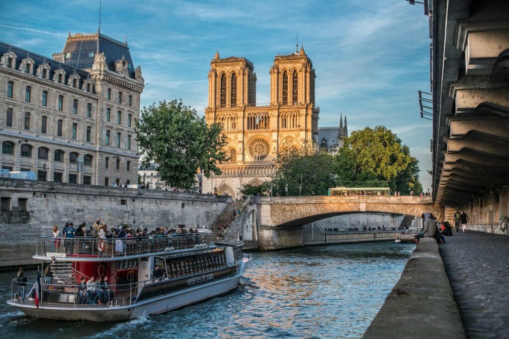 Um barco navega no Rio Sena perto da Catedral de Notre-Dame, em Paris, com edifícios históricos e uma ponte ao fundo.