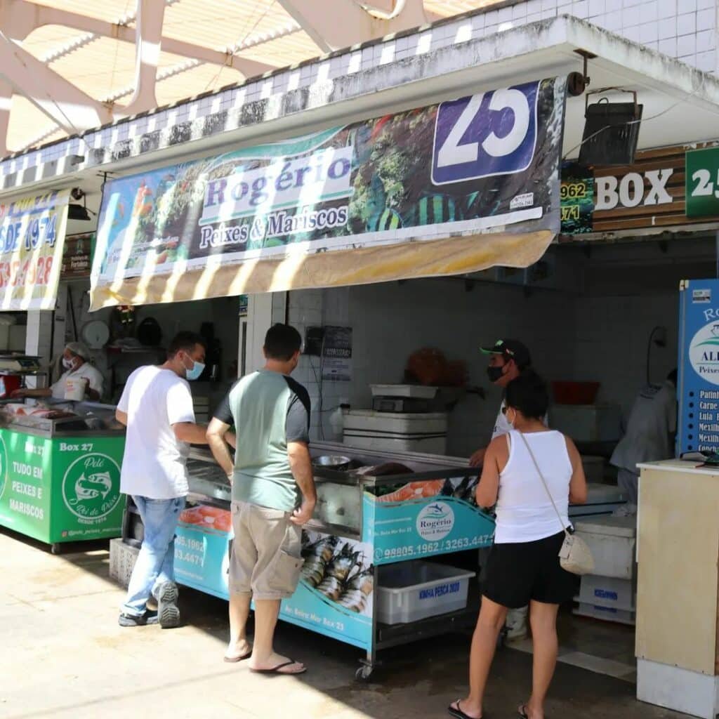 Pessoas comprando no Mercado dos Peixes em Fortaleza. Estão escolhendo suas peças e há várias lojas uma ao ado das outras.