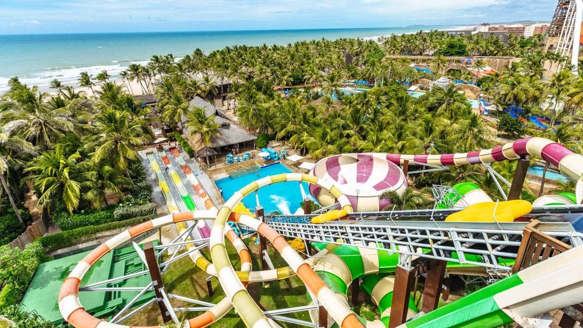 Foto aérea do Beach Park. Vê-se os toboáguas coloridos, várias palmeiras, uma piscina e a praia no fundo.