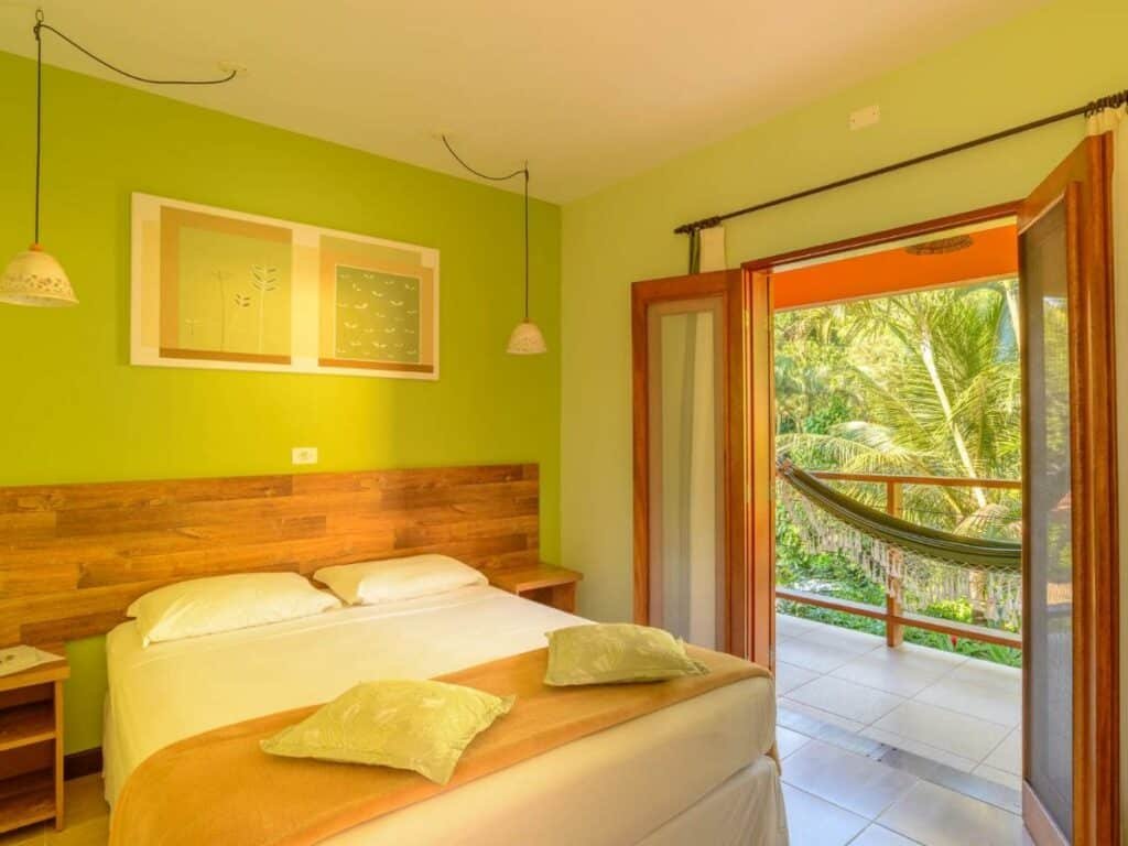 Quarto da Pousada Ecoilha, em Ilhabela, com pendentes sobre as mesas de cabeceira e varanda com rede