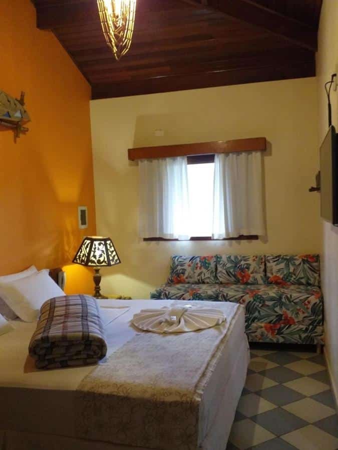 Quarto com cama de casal, abajur, TV e sofá na Pousada Maui