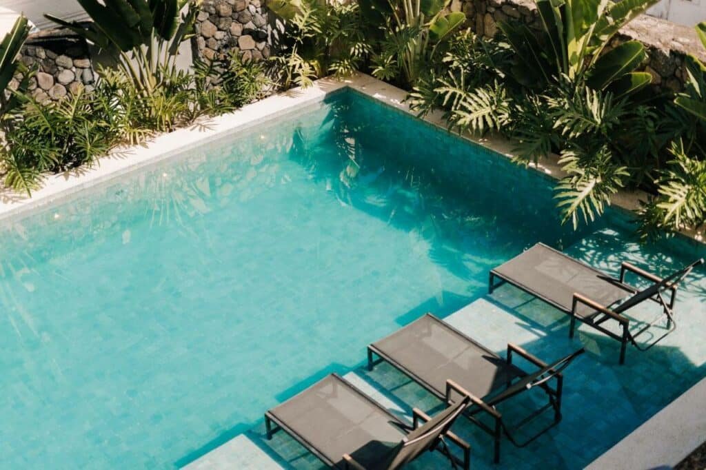 Vista de cima de espreguiçadieras dentro da piscina da Pousada Zama, que é cercada por plantas.