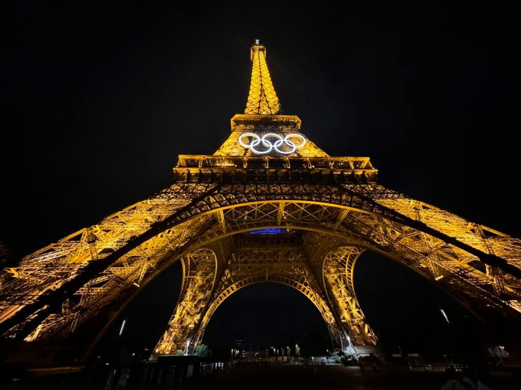 A Torre Eiffel iluminada à noite, com os anéis olímpicos expostos com destaque perto do topo. Esse é um dos pontos turísticos de Paris.