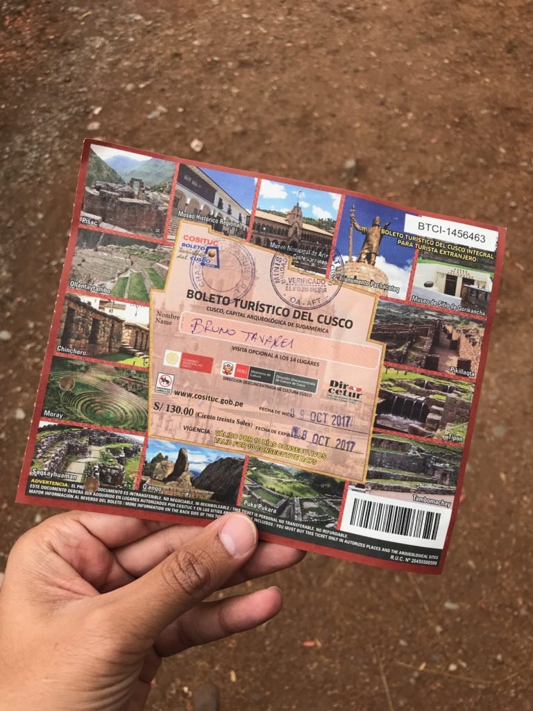 papel do Boleto turístico com várias atividades descritas sobre o que fazer em Cusco. Uma mão masculina e morena segura o papel para a foto.