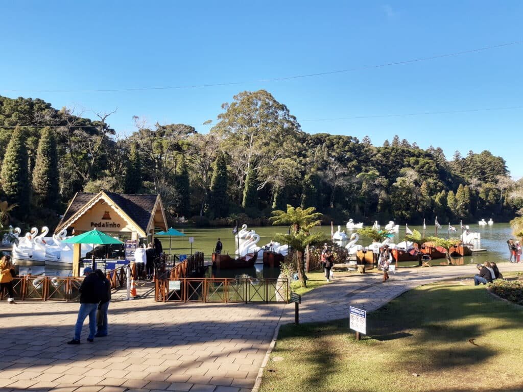 entrada do parque lago negro com vista para o porto do lago onde ficam vários pedalinhos em formato de cisne branco. O céu está azul claro e sem nuvens