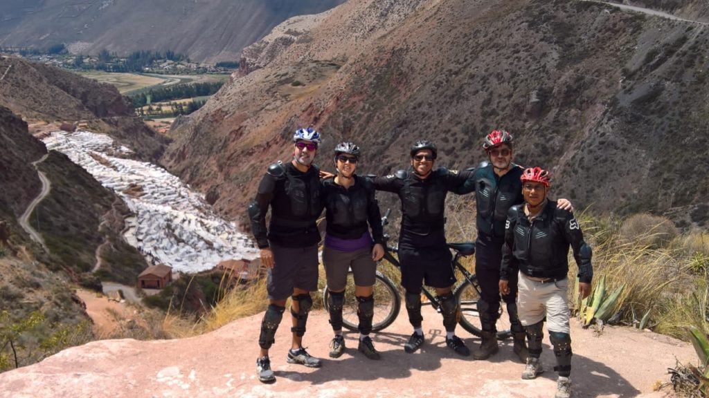 Cinco amigos posando para a foto, que mostra as salineras de maras ao fundo. Todos estão sorrindo e abraçados