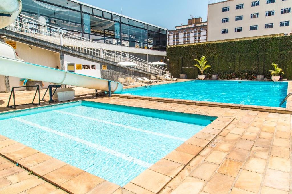 Piscina do Hotel Metrópole. É possível ver duas piscinas (uma mais rasa e menor do que a outra) um toboágua, guarda-sóis e vasos com plantas.