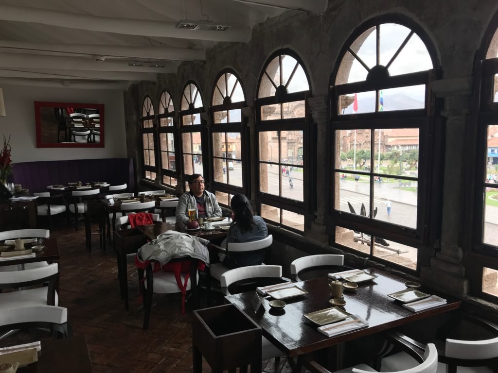 interior do Restaurante Limo em Cusco com várias mesas com quatro cadeiras ao lado de várias janelas com vista para a plaza de armas