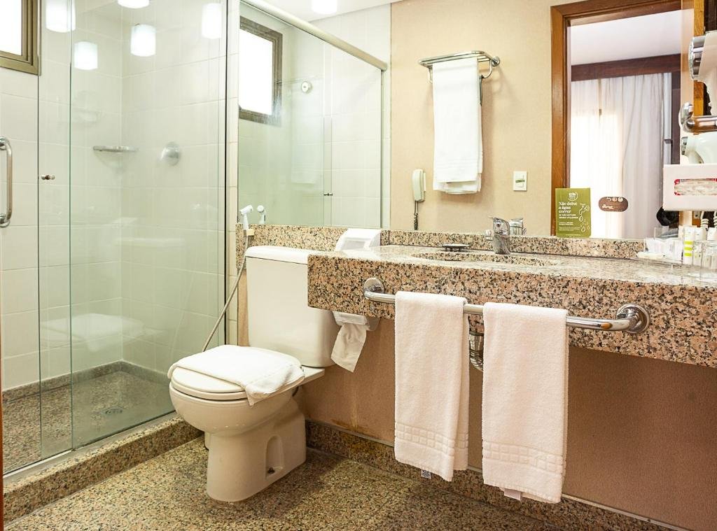 Imagem do banheiro de um dos quartos do Mercure Belo Horizonte, para representar o post de hotéis com piscina aquecida em Minas Gerais. O banheiro possui barras de apoio no box do chuveiro e na pia, na qual há algumas amenidades disponíveis em sua superfície. A privada está entre a pia e o box.