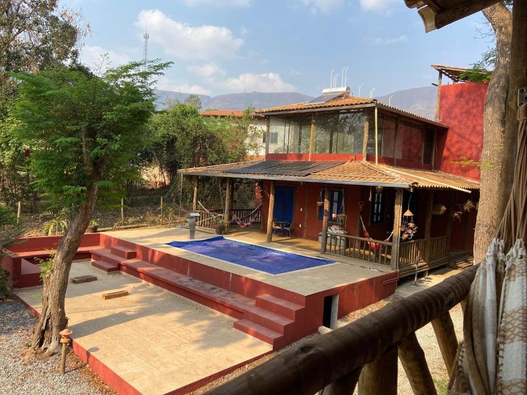 Área externa da A Mi Manera Bistro, uma das pousadas em Macacos, com uma área de piscina, e varanda do edifício com algumas redes. Há alguns degraus dando acesso a uma área de descanso e bastante natureza em volta