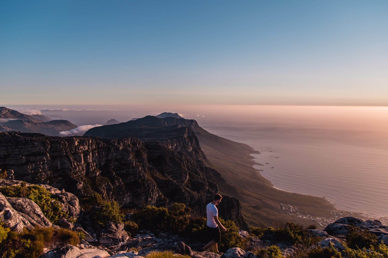 Homem caminhando em uma trilha em meio à costa montanhosa da Cidade do Cabo, na África do Sul. Logo abaixo fica a praia. - Foto: Arthur Brognoli via Pexels