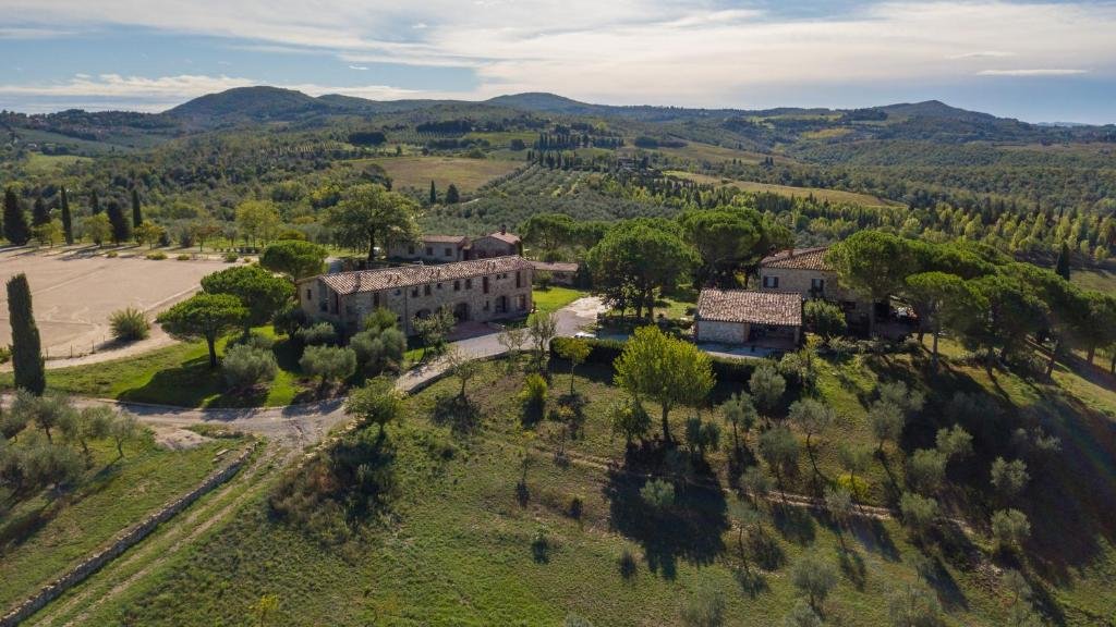 Vista aérea de um dos hotéis na Toscana, o Agriturismo Sole, com muita vegetação verde em volta e alguns prédios de tijolos a vista da propriedade