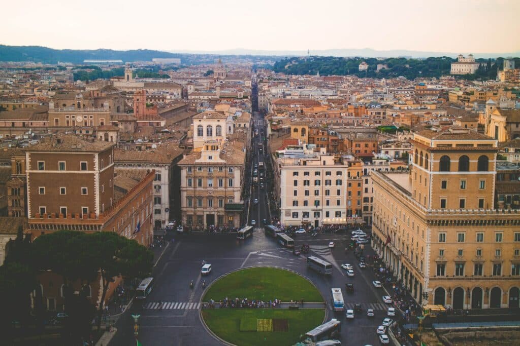 vista de cima de uma via com vários carros e ônibus com uma rotatória no centro da Altare della Patria, em Roma, com vários prédios ao redor