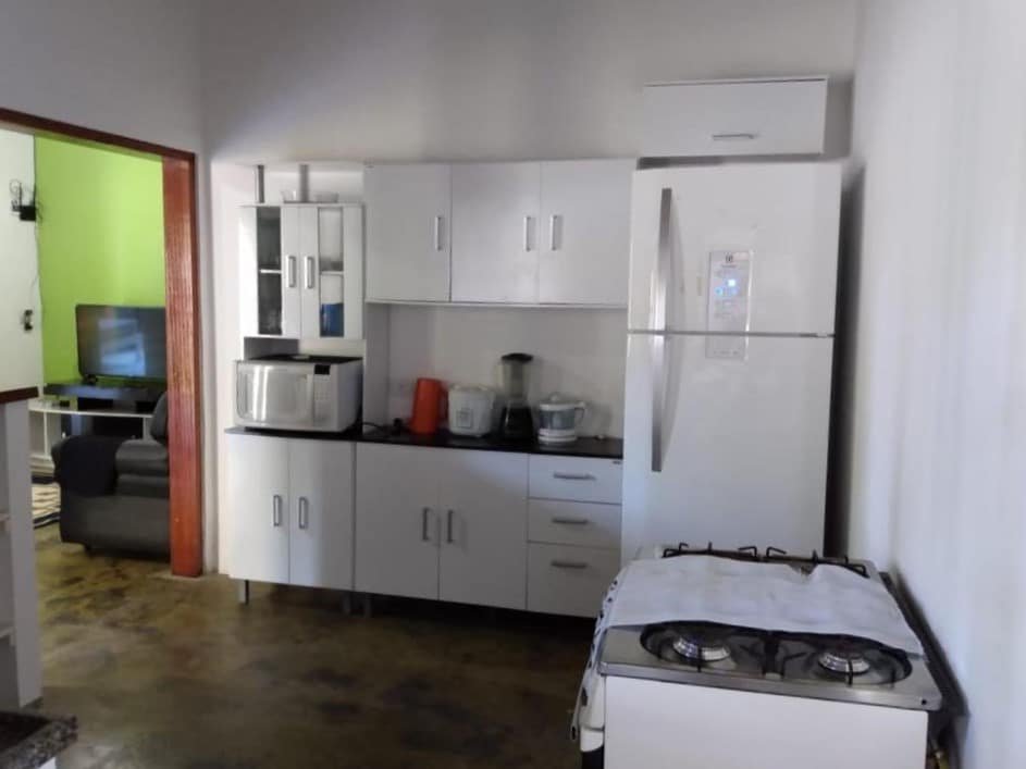 Cozinha do Aluguel temporário. Do lado direito um fogão, no fundo uma geladeira. No meio um armário com micro-ondas e utensílios de cozinha. Do lado esquerdo a porta da sala.