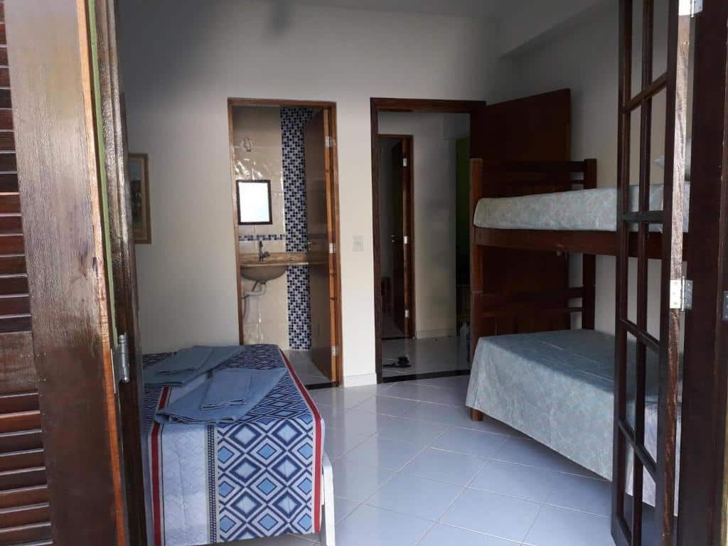 Quarto do Aluguel temporário. Do lado esquerdo uma cama de casal, no fundo um espelho e a porta do banheiro aberta. Do lado direito uma cama beliche e no fundo a porta do quarto aberta. Na frente, a porta da varanda aberta dando vista para o quarto. Foto para ilustrar post sobre airbnb em Perequê Mirim.
