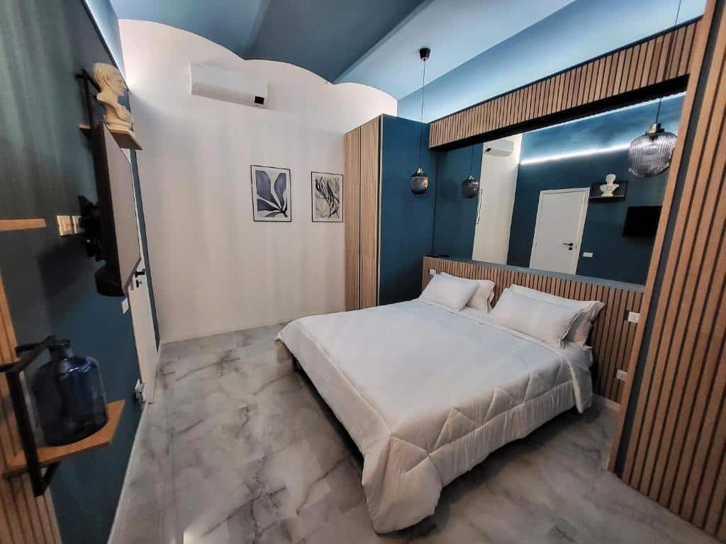 quarto com cama de casal, decoração branca com detalhes em verde, tv e luminária no DrsRome - Roman