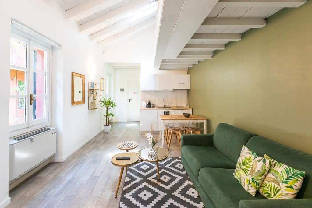 Sala de estar e cozinha do Alzaia Naviglio Grande há um sofá com almofadas e uma mesa de centro com um vaso de flor, depois há uma mesa de quadro lugares e uma pequena cozinha