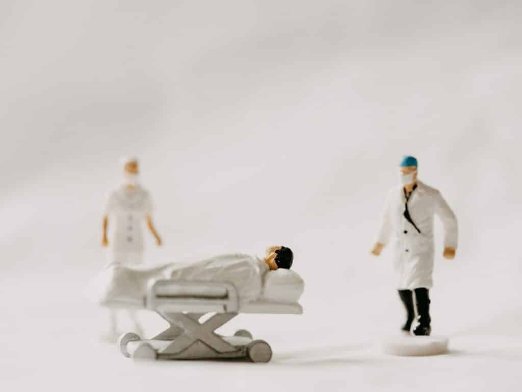 Três bonecos pequenos com roupas de médico, sendo uma enfermeira, um médico e um paciente deitado em uma maca