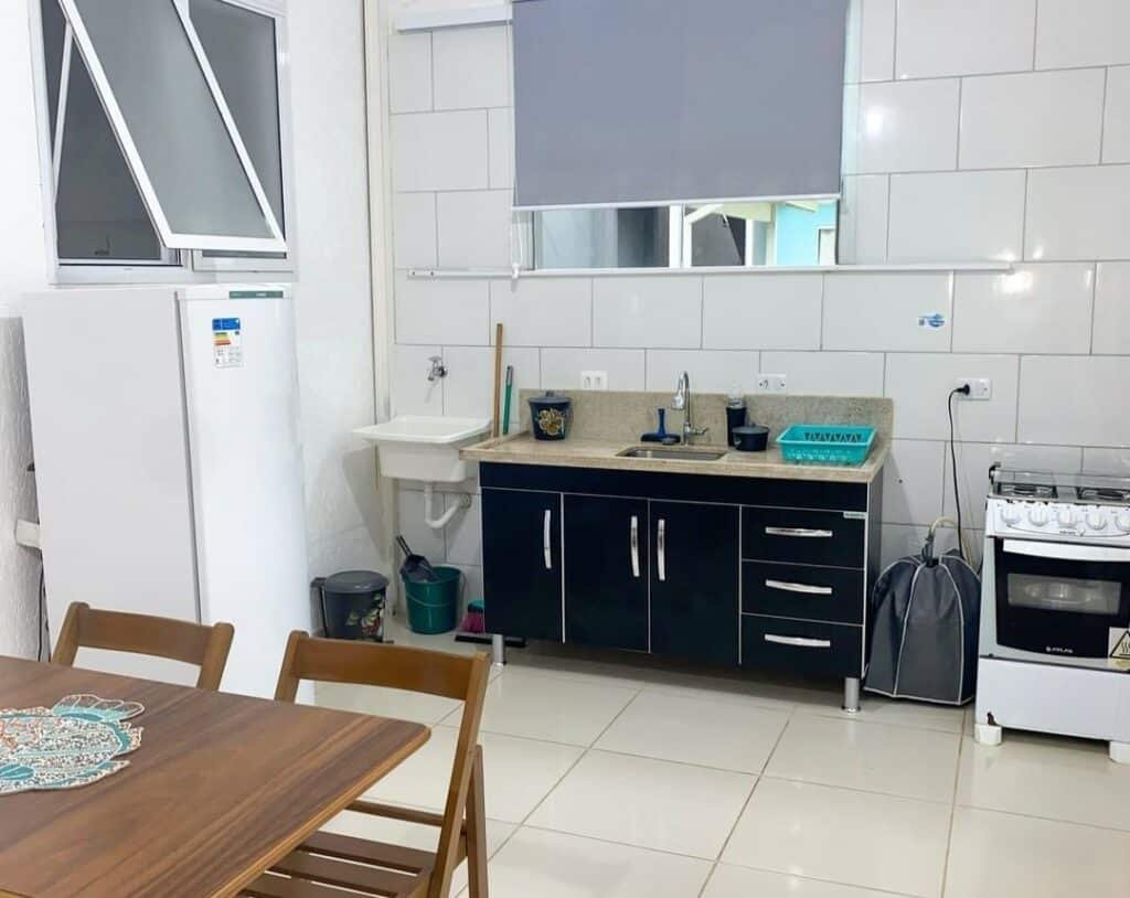 Cozinha de um dos Apartamentos da 23. A pia está ao fundo, do lado de um pequeno tanque e de um fogão. Na parede ao lado está geladeira. Em primeiro plano é possível ver uma mesa.