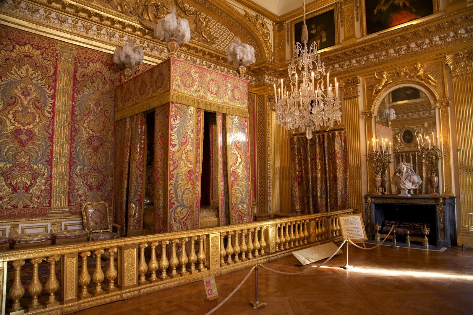 Sala ornamentada com decoração dourada, grandes tapeçarias, lustre de cristal e lareira de mármore. Barreira de corda em primeiro plano. É um dos apartamentos do Rei no Palácio de Versalhes.