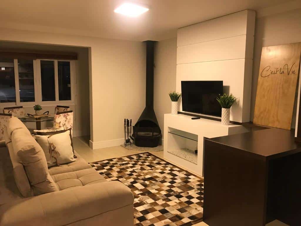 Sala no Apto. Baviera. O sofá está no canto inferior esquerdo da foto. na sua frente há uma lareira e televisão. No fundo da foto, à esquerda há uma mesa com quatro cadeiras e uma janela atrás.