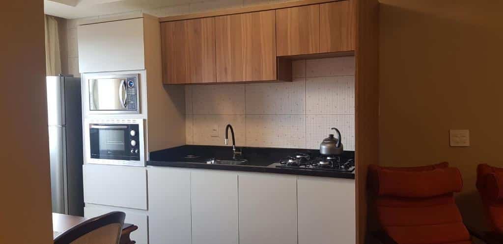 Cozinha no Apto Bell Canela "Cobertura no Centro". Vemos gabinetes modernos, uma pia, cooktop, micro-ondas, forno e geladeira.