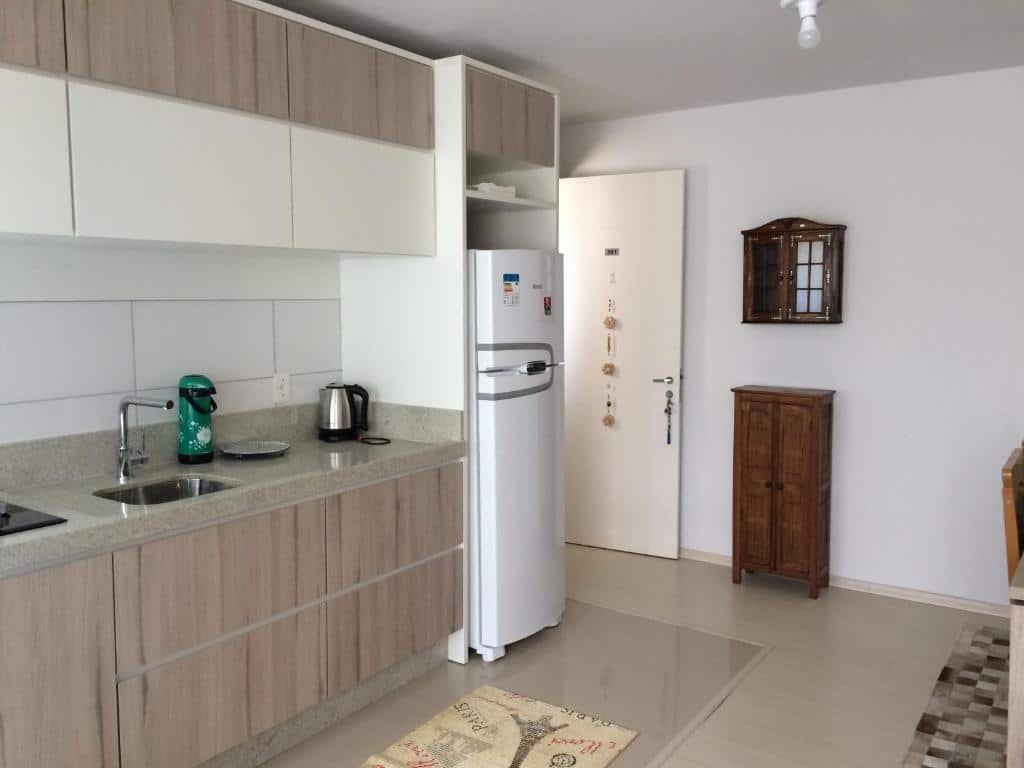 Cozinha do Serenidade em Canela. Os armários, pia e geladeira estão à esquerda, e uma porta também. Um armário de chão e outro de parede estão à direita.