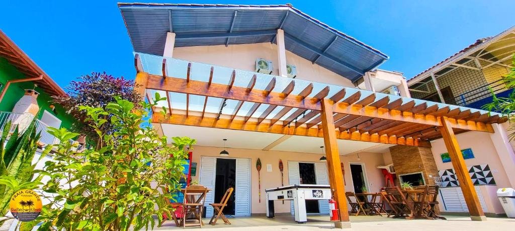 Entrada da Pousada Praia Grande Hostel, um local amplo, com algumas plantas, uma armação de madeira que protege uma mesa de sinuca, uma churrasqueira, algumas cadeiras e mesas