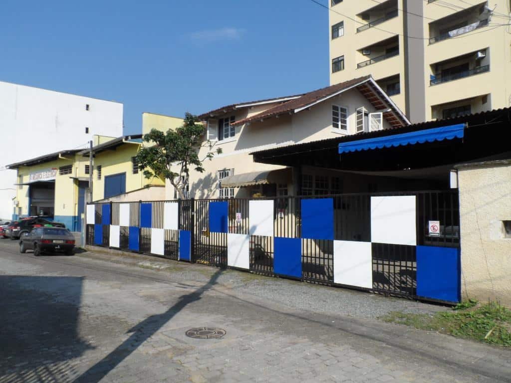 Rua onde fica a Austria Hostel & Pousada com um portão de grade preto, com alguns quadrados brancos e azuis e uma árvore no lado de dentro