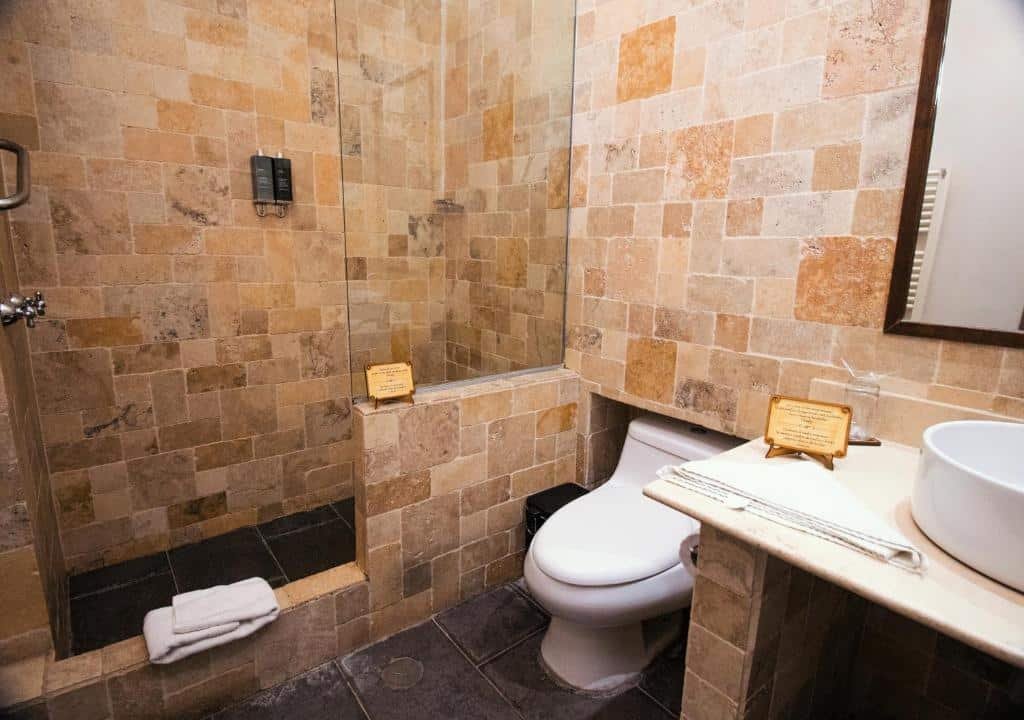 banheiro do Tambo del Arriero Hotel Boutique em Cusco com a parede toda coberta por pedras, um box espaçoso e uma pequena pia no canto inferior direito.