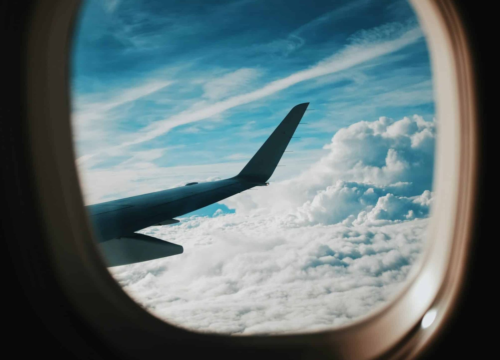 Vista da janela do avião mostrando a asa, com um céu azul e nuvens brancas abaixo. A imagem ilustra o post sobre como chegar em Paris.