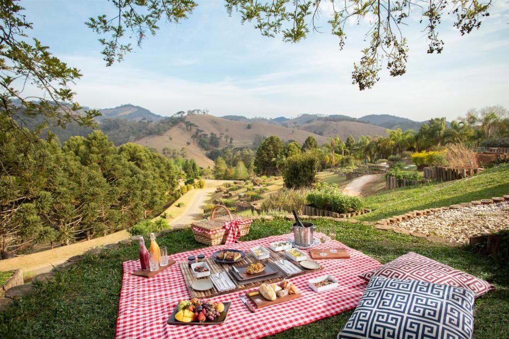 Piquenique montado em uma colina com um cobertor xadrez vermelho, comida e bebidas. Com vista para uma paisagem cênica com árvores e colinas distantes.