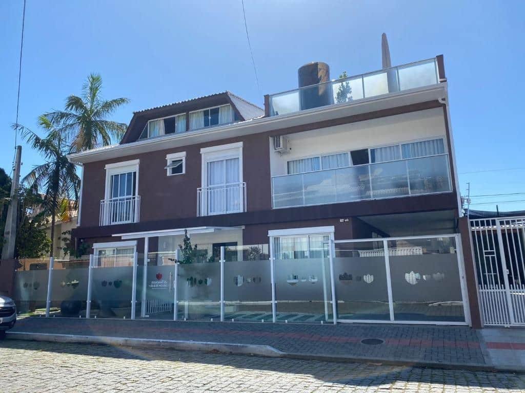 Frente da Bouganville Guest House, com portão de vidro, paredes marrom e algumas portas no segundo andar com sacada para ilustrar as pousadas em Balneário Camboriú