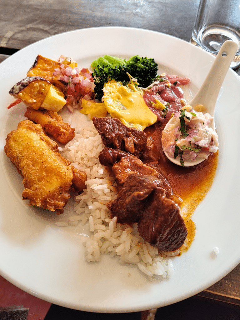 prato circular branco com vários alimentos, como arroz, carne de alpaca, mandioca frita, legumes (brócolis e batata doce) e uma colher de ceviche do restaurante Tunupa no Vale Sagrado dos Incas