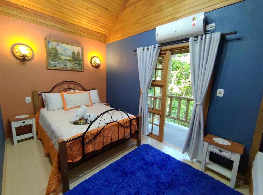 Foto do interior da Cabana Drechsler Gramado representando o post de chalés em Gramado. O quarto é espaçoso e conta com uma cama de casal. Do lado direito da cama há uma porta com varanda,, e acima dela há um ar-condicionado.
