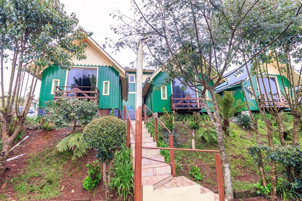 Pousada Cabanas Brisa dos Canyons em Cambara do Sul com três chalés verdes no alto do morrinho. É possível acessar através de uma escada de piso branco no jardim