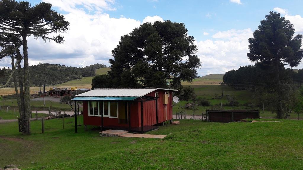 Cabana do Casarão vermelha no meio de um gramado verde com algumas árvores ao redor e uma vista da serra ao fundo