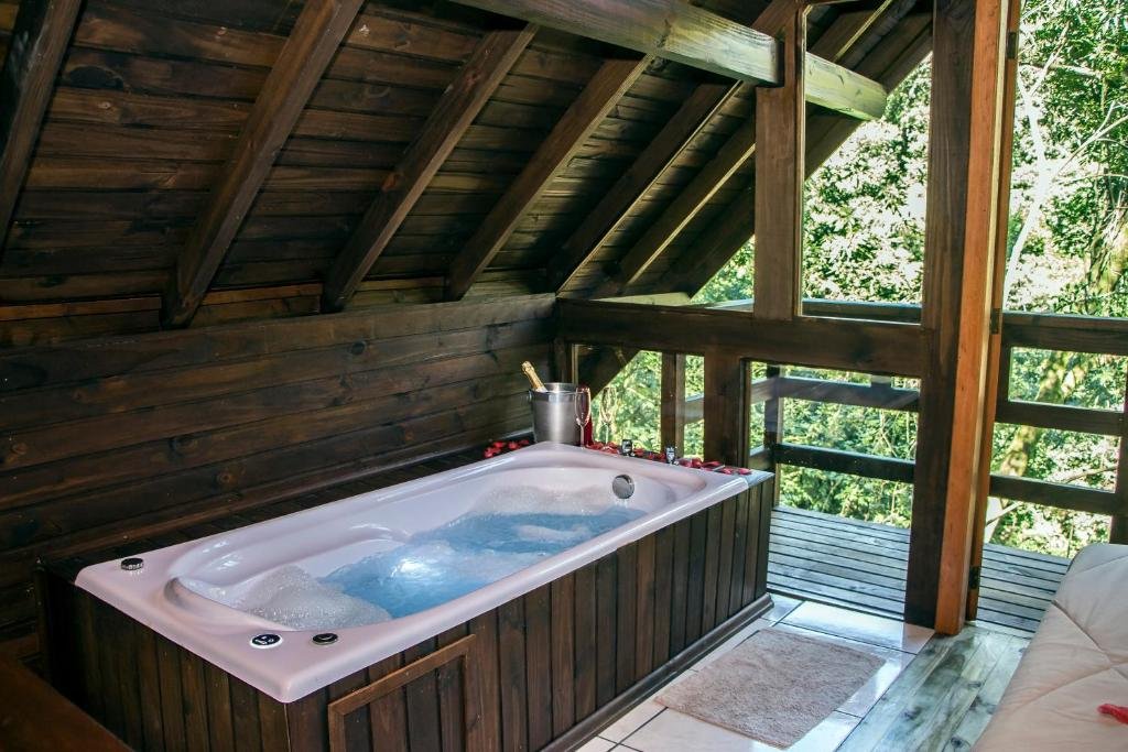 Uma banheira de hidromassagem na Cabana dos Plátanos. Atrás dela há uma varanda com vista para a mata.
