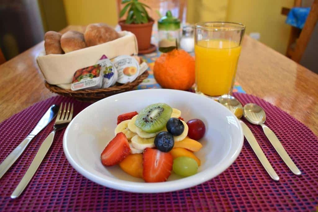mesa de café da manhã do Pisac Inca Guest House com uma prato branco com frutas picaadas dentro, além de uma cesta de pães e um copo de suco de laranja