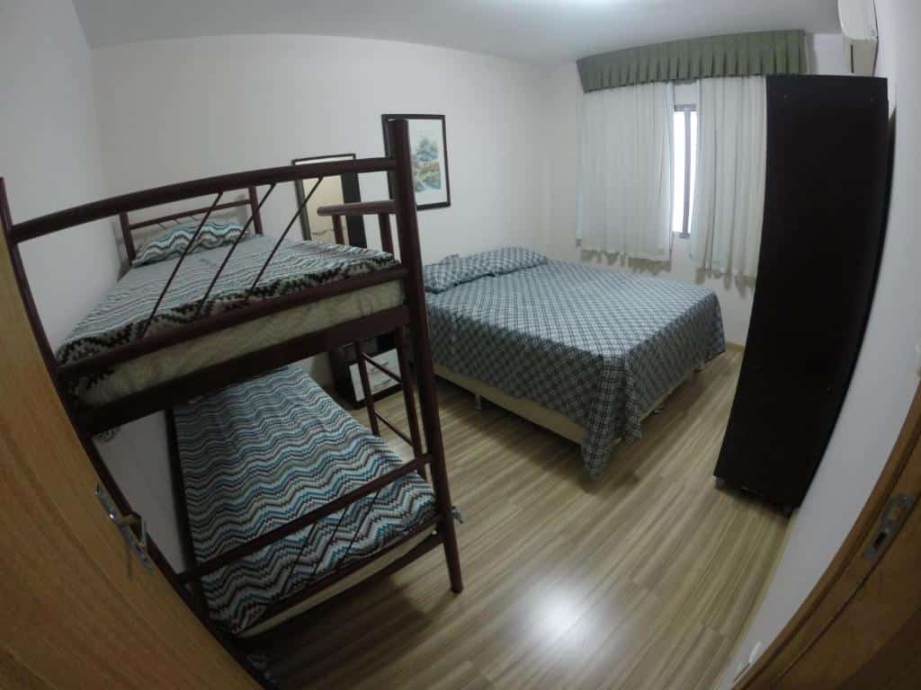 Quarto da Casa Área Central. Do lado esquerdo uma cama beliche, do lado direito uma cama de casal com um armário de frente e no fundo a janela do quarto. Foto para ilustrar post sobre airbnb em Balneário Camboriú.