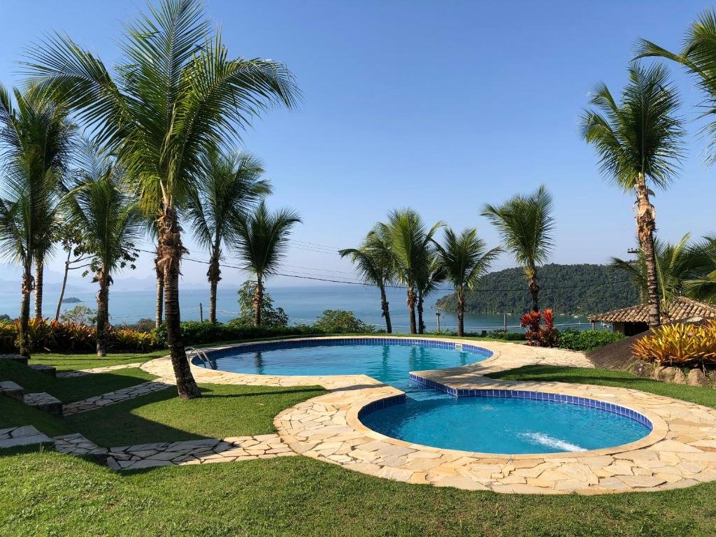 Área externa da Casa com vista para o mar!. Uma piscina no meio, com uma piscina menor e outra grande, ao redor o jardim e palmeiras, no fundo a vista do mar.