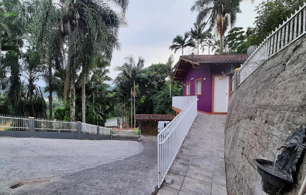 Entrada com um caminho íngreme para dar acesso à Casa da Maga, uma das pousadas em Blumenau. No lado esquerdo há várias árvores e no direito uma pequena fonte descendo água