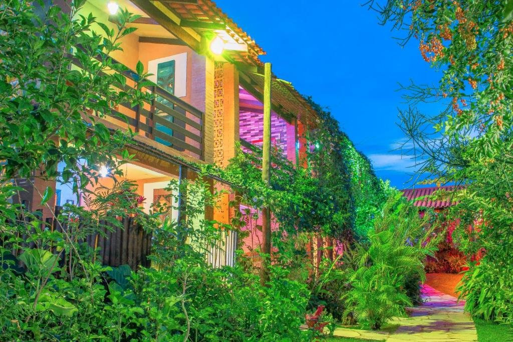 Faixada da Pousada Casa de Frida Pousada Galeria, muita vegetação ao entorno, as sacadas dos quartos iluminadas e caminho de pedras na área externa. 