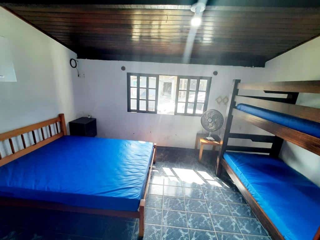 Quarto da Casa 45 Estaleiro. Uma cama de casal do lado esquerdo, no fundo a janela do quarto, do lado direito uma cama beliche e um ventilador.