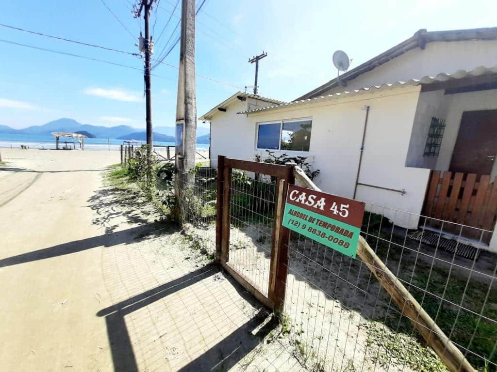 Área externa da Casa 45 Estaleiro. Do lado direito a casa, no meio um cercado, do lado esquerdo o caminho de areia com vista da praia.