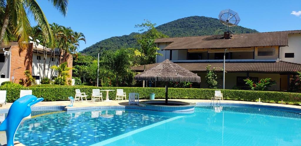 Área externa da Casa Melo 4. Uma piscina com uma ilha de quiosque e cadeiras de praia ao redor. Ao redor um jardim e no fundo prédios. Do lado esquerdo uma cascata de golfinho.