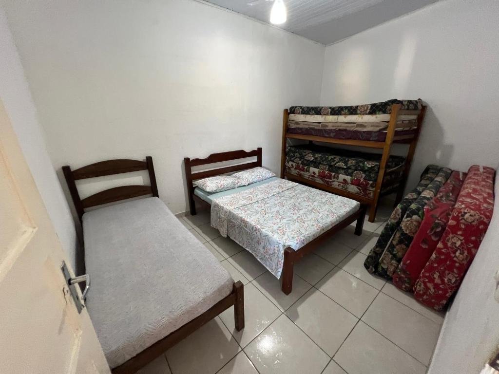 Quarto da Casa Temporada. Do lado direito quatro colchões em pé. Do lado esquerdo uma cama de solteiro, uma cama de casal e uma cama de beliche no fundo com diversos colchões. Foto para ilustrar post sobre airbnb em Perequê Mirim.
